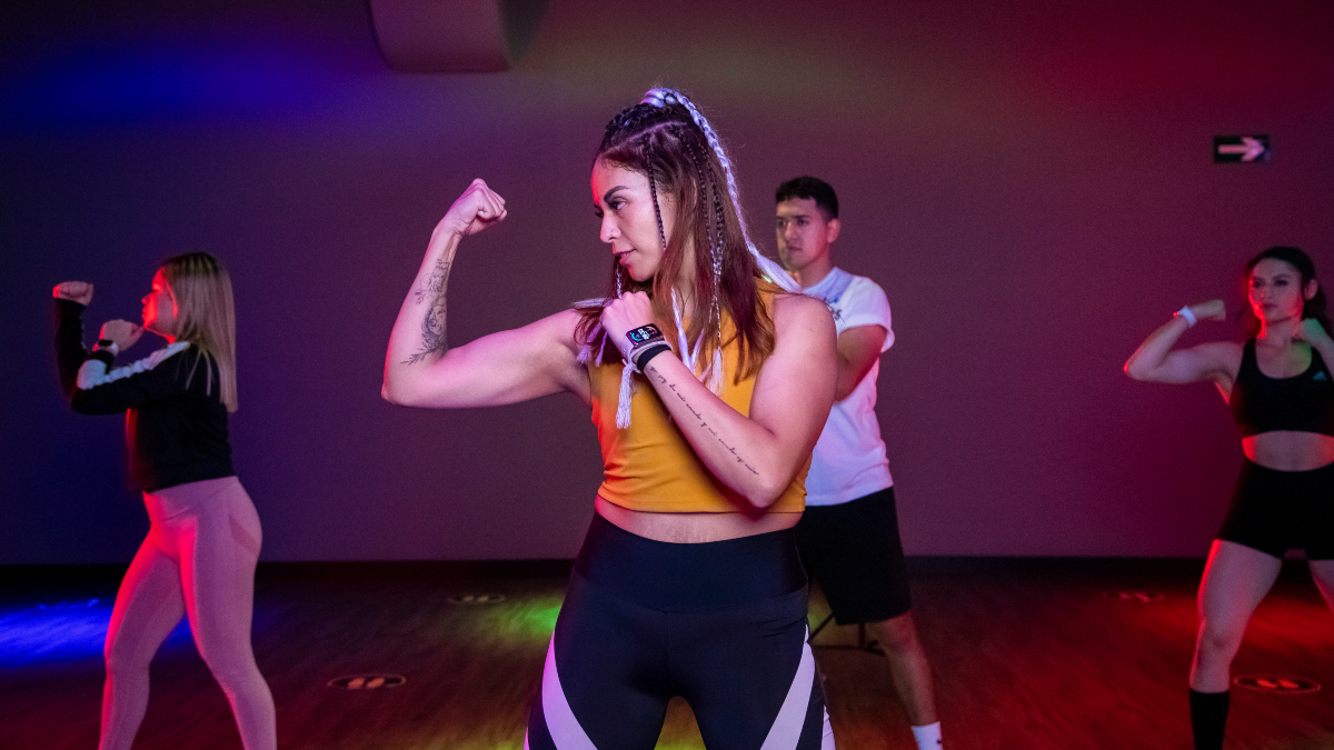 mujer de perfil en primer plano, en posición de guardia de boxeo. Dos mujeres y un hombre en la parte posterior en posición de guardía también, tomando una clase de Body Combat en Smart Fit.