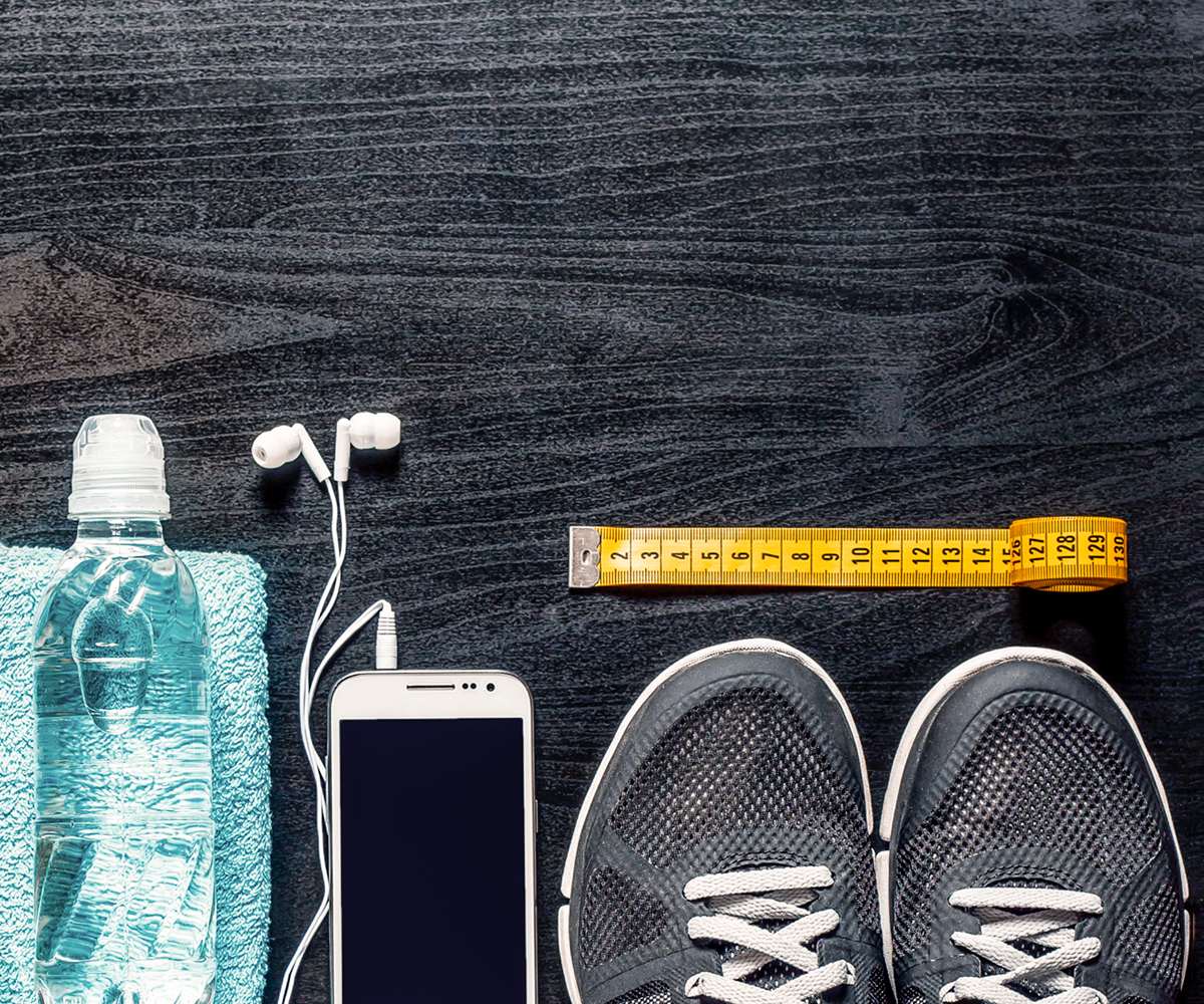 par de tenis, un teléfono con audifonos conectados, una toalla con una botella de agua encima y una cinta métrica