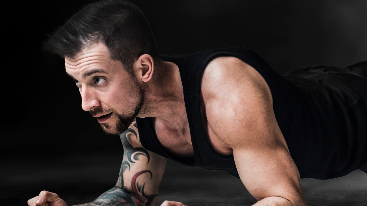 torso de un hombre recostado boca abajo en el suelo, con los antebrazos apoyados en el piso y la mirada al frente