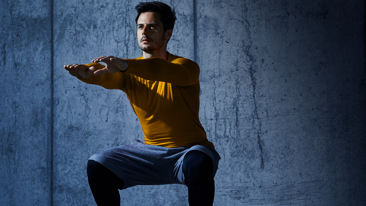 hombre con las rodillas flexionadas en posición de sentadilla, con los brazos extendidos hacia el frente