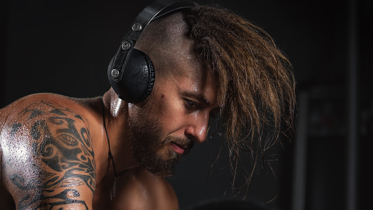 parte superior de un hombre con la cabeza agachada y la mirada al suelo, con unos audifonos cubriendo sus oídos.