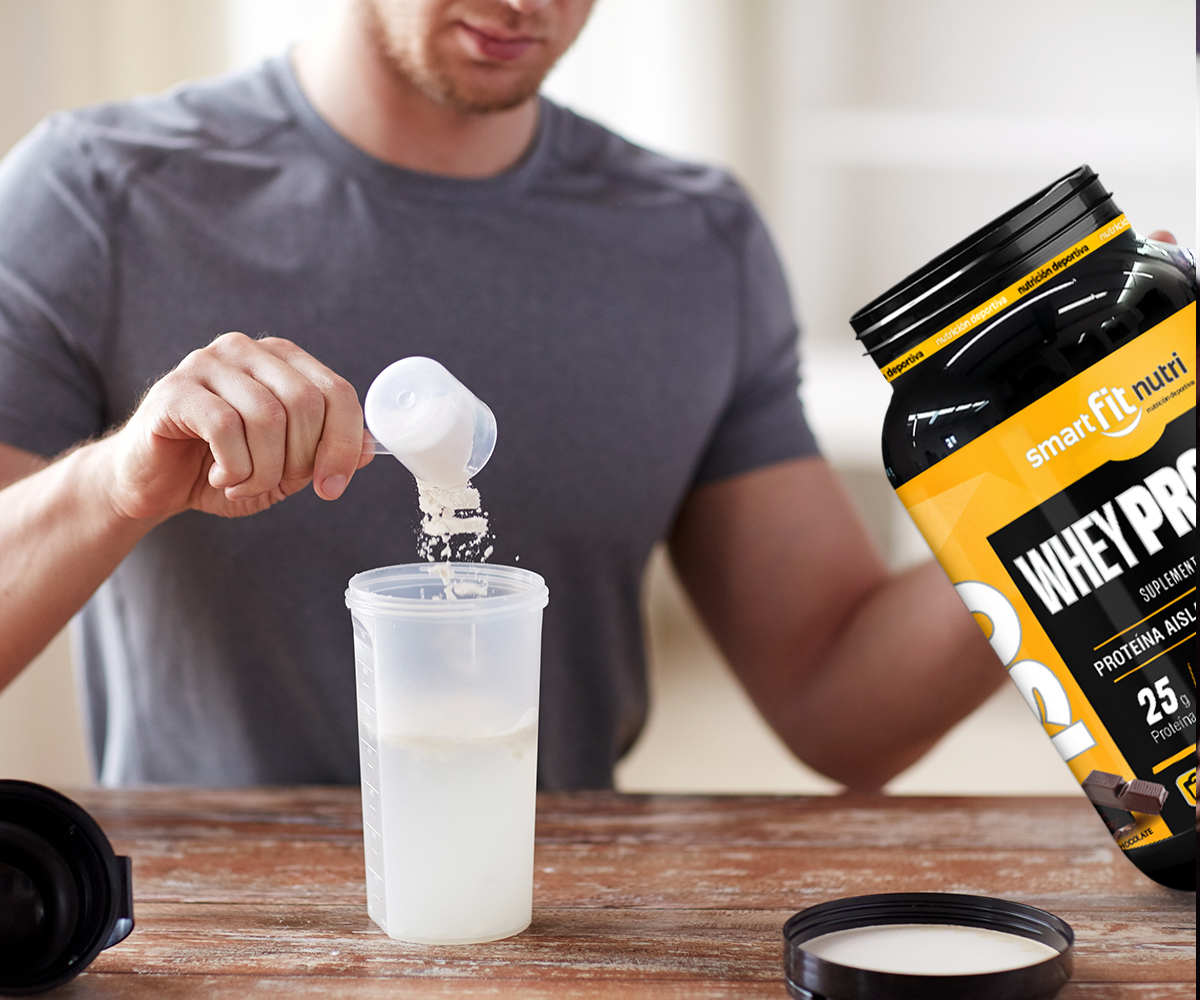 Hombre agregando un scoop de proteína en polvo en un vaso. En la otra mano sostiene un bote de uno de los suplementos alimenticios de Smart Fit Nutri