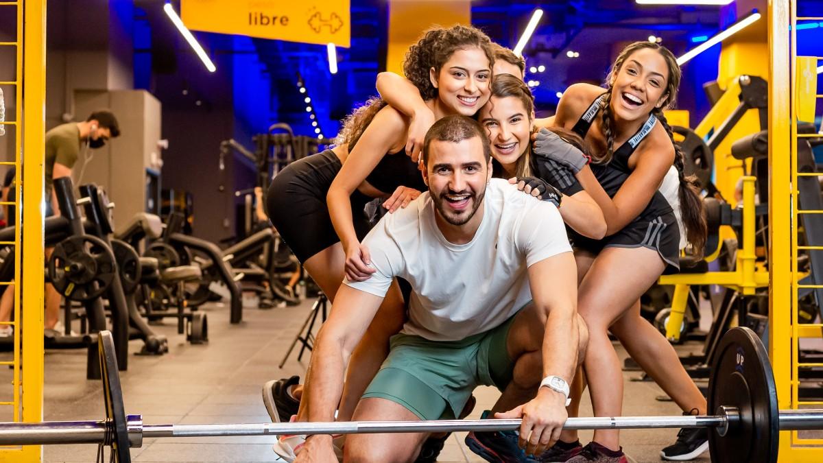 cinco usuarios de un gimnasio smart fit agachados y posando para una fot, con las caras sonrientes