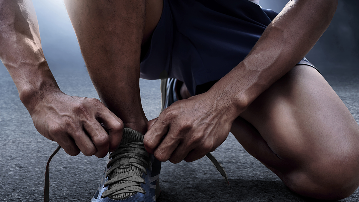 manos de una hombre con ropa deportiva amarrandose las agujetas de sus tenis.