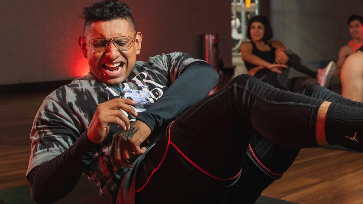 hombre sentado en el piso con el torso inclinado hacia atras y las piernas levantadas, en el rostro una expresión de dolor