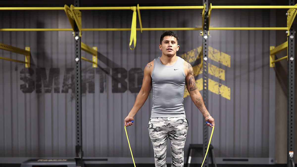 hombre de pie saltando una cuerda que tiene sostenida con una mano en cada extremo