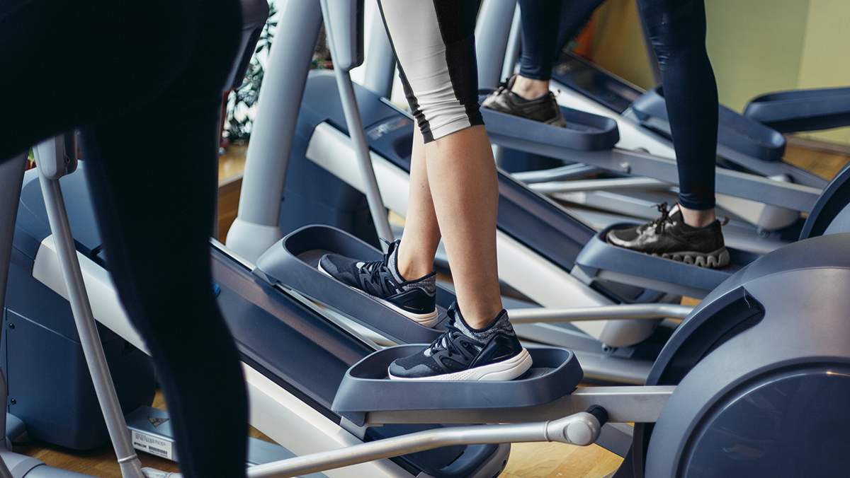 piernas de tres mujeres paradas en la maquina elpitica de un gimnasio