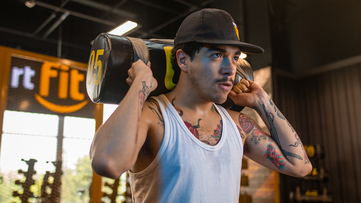 torso de un hombre sosteniendo con las dos manos un saco de arena en los hombros