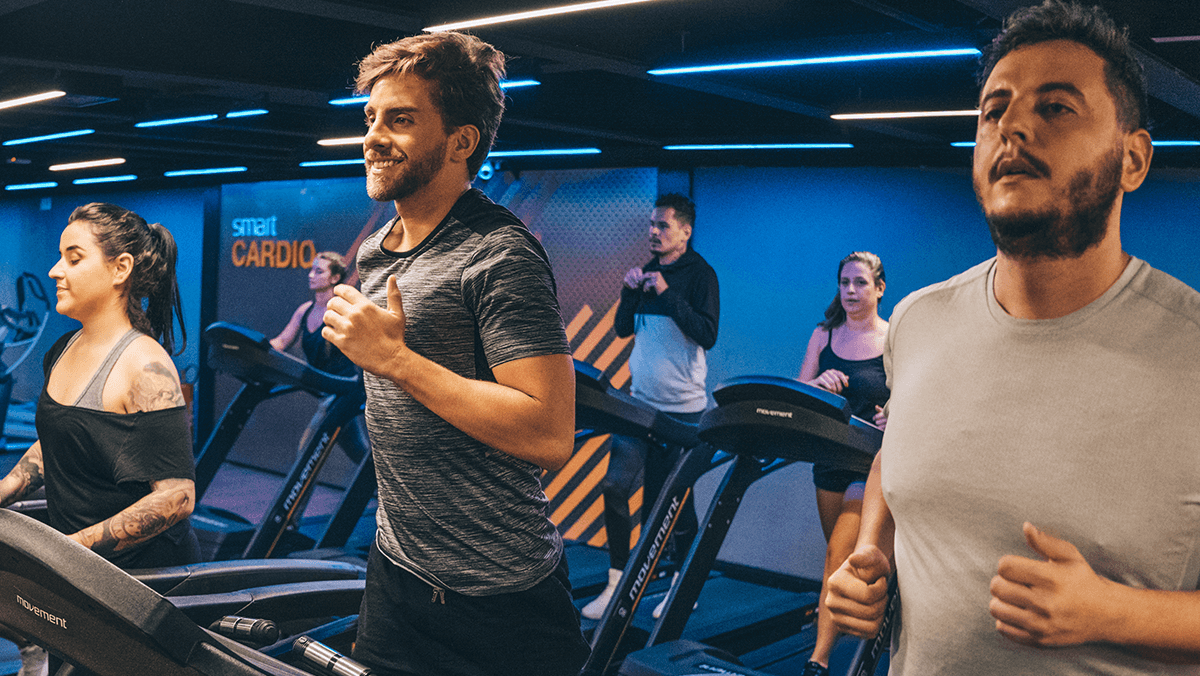 torsos de dos hombres y una mujer corriendo en las caminadoras de un gimnasio smart fit