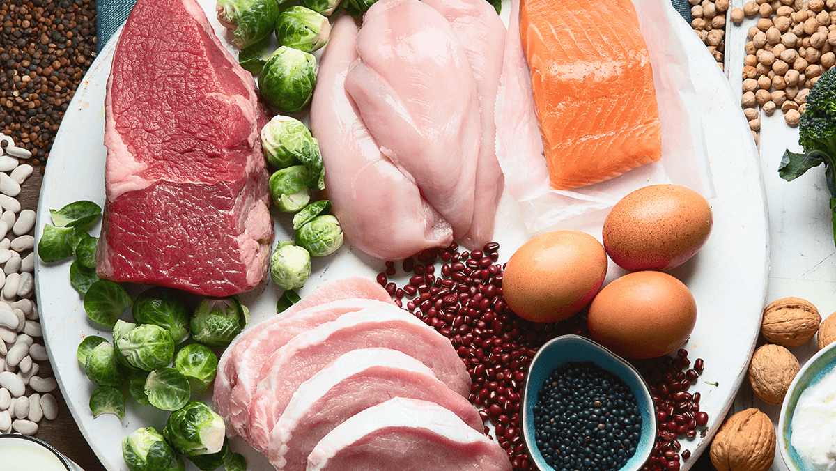 vista en contrapicada de un plato con un pedazo de carne de res, dos pedazos de pechuga de pollo, y trozo de salmon, tres huevos, y legumbes