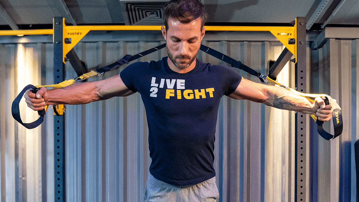 torso de un hombre de frente, ligeramente inclinado hacia el frente con los brazos extendidos hacia los lados sosteniendo en cada mano una cuerda trx