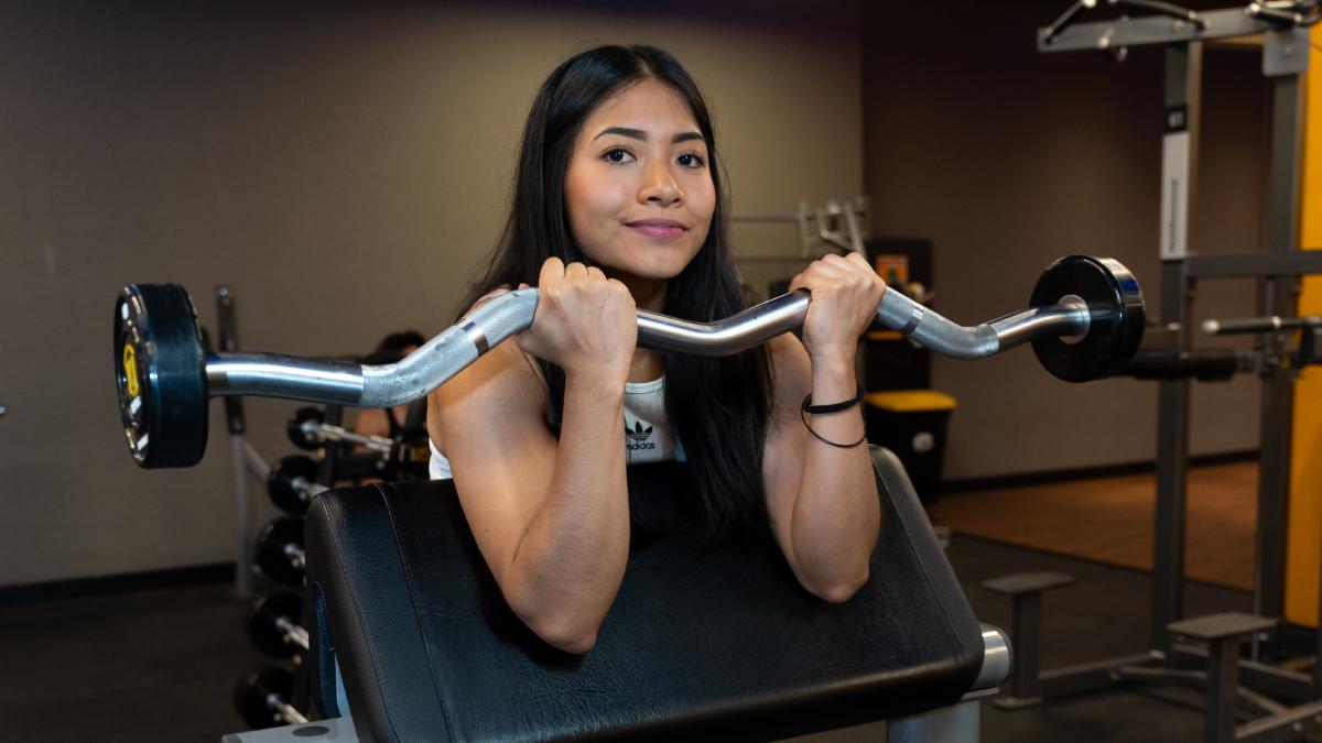 torso de una mujer de frente, posicionada en un banco scott, realizando un curl predicador