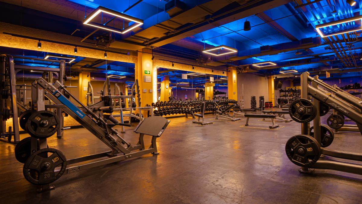 vista del area de peso libre de un gimnasio smart fit en guadalajara con dos prensas para pierna en primer plano y mancuenras, barras discos y bancos en segundo plano