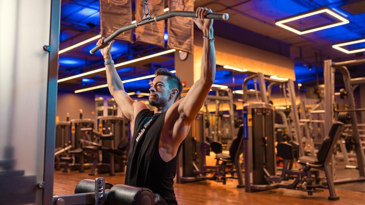 Persona realizando un jalon en polea vertical, trabajando patrones de movimiento esenciales en un gimnasio Smart Fit, con un entorno moderno y equipos de alta calidad.