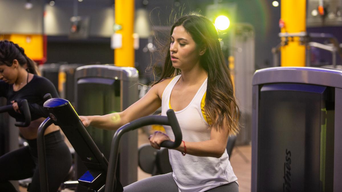 mitad del cuerpo de una mujer en una elíptica en el gimnasio. con una mano ajustando la máquina y la otra sostenida en el soporte.