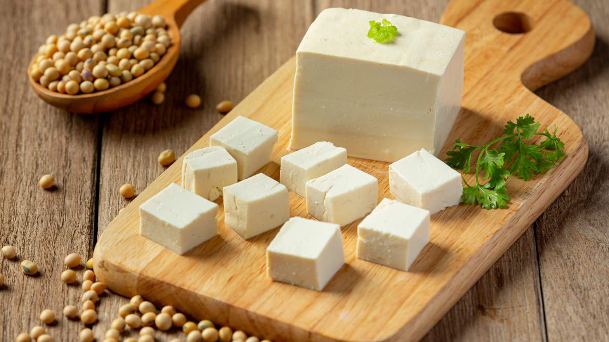 Tabla sobre una mesa con pedazos de tofu y semillas