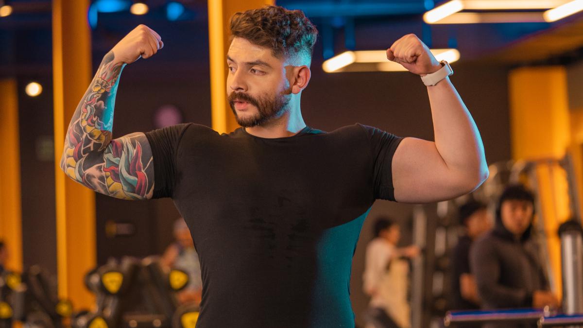 hombre de pie con los brazos flexionados hacia los costados esneñando sus músculos bíceps