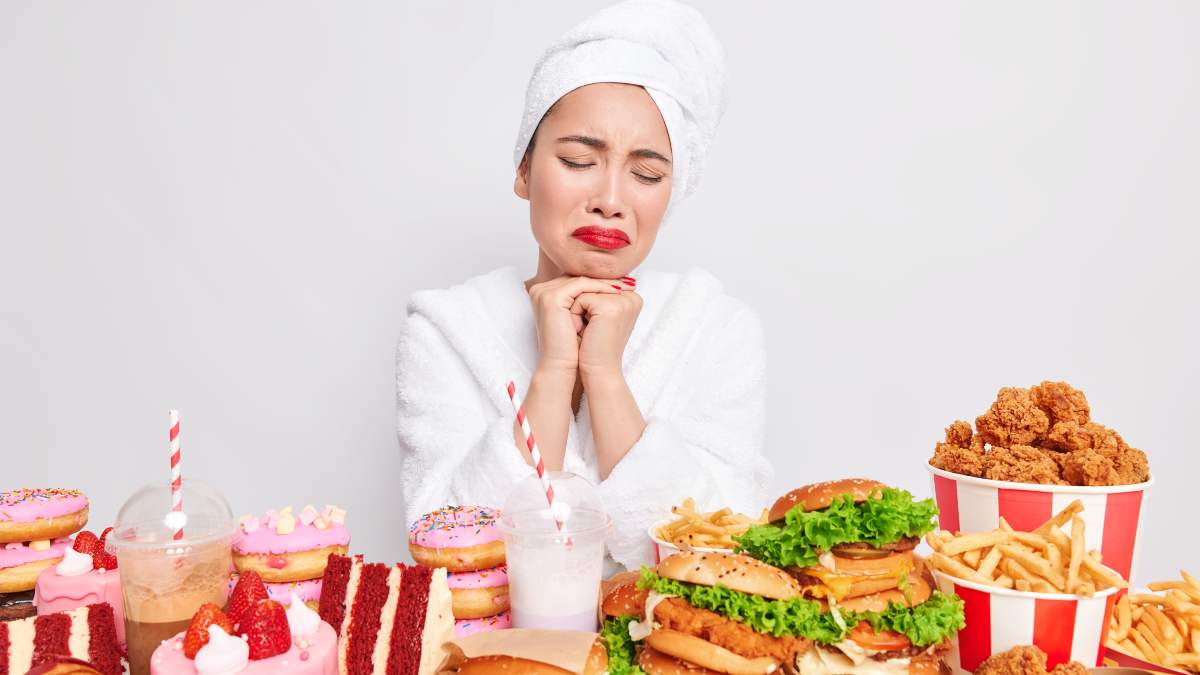 mujer frente a una mesa llena de comida procesada con rostro de sufrimiento por la tentación de caer en un atracón de comida