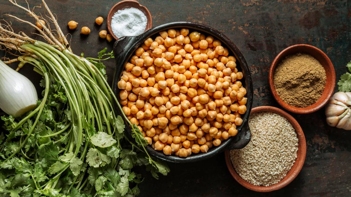 bowl sobre una mesa lleno de garbanzos, con más cereales y legumbres alrededor