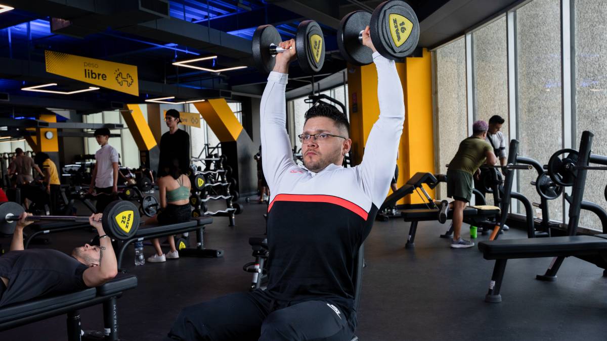 hombre sentado en un banco del gimnasio realizando un press militar con mancuernas