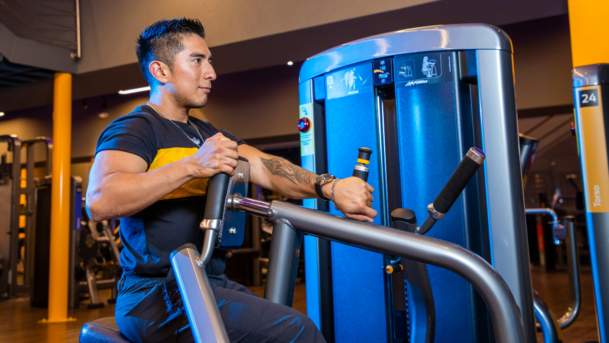 hombre sentado en una máquina de peso integrado, realizando un ejercicio para aumentar masa muscular