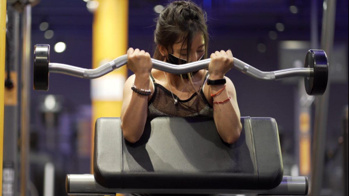 mujer sosteniendo una barra z sobre un banco scott, realizando un curl predicador.