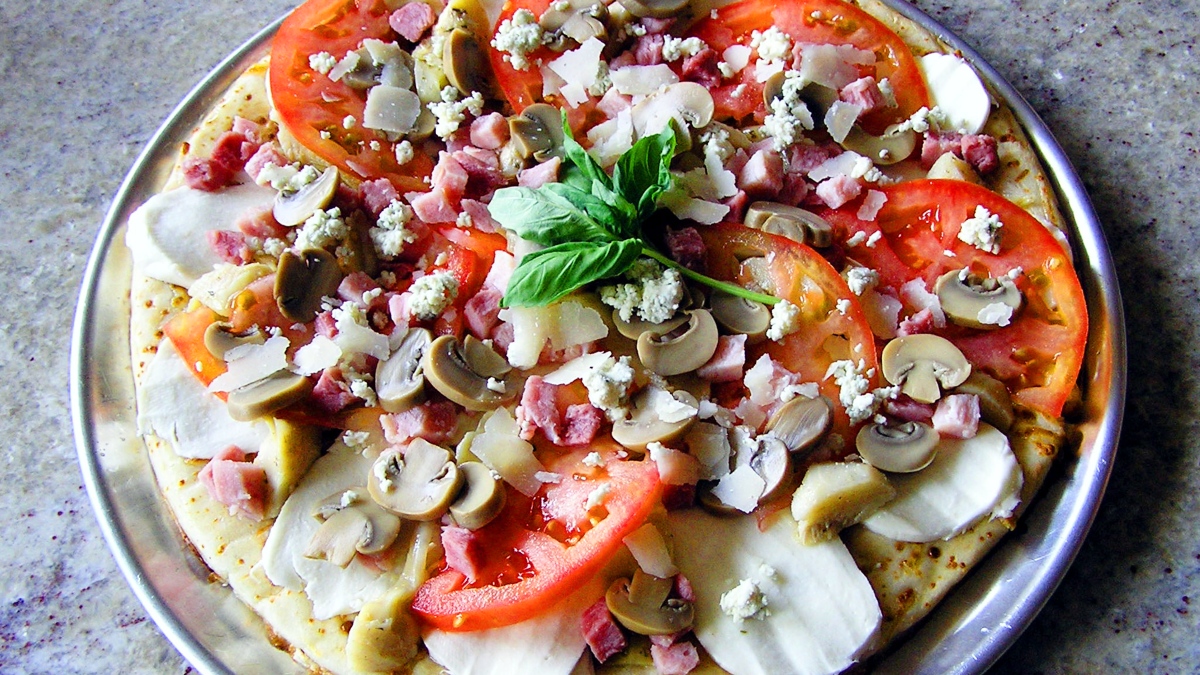 charola en una mesa con una pizza saludable elaborada con rebanadas de queso oaxaca, jitomate, champiñones y pedazos de carnes frías