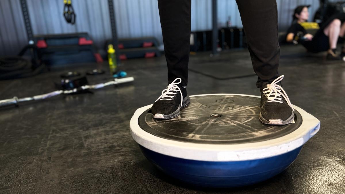 Dos piernas y pies pisando la parte plana de una pelota bous en el gimnasio Smart Fit