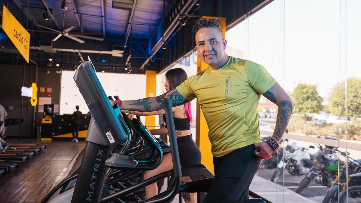 hombre parado en una caminadora del gimnasio Smart Fit, volteando a la cámara