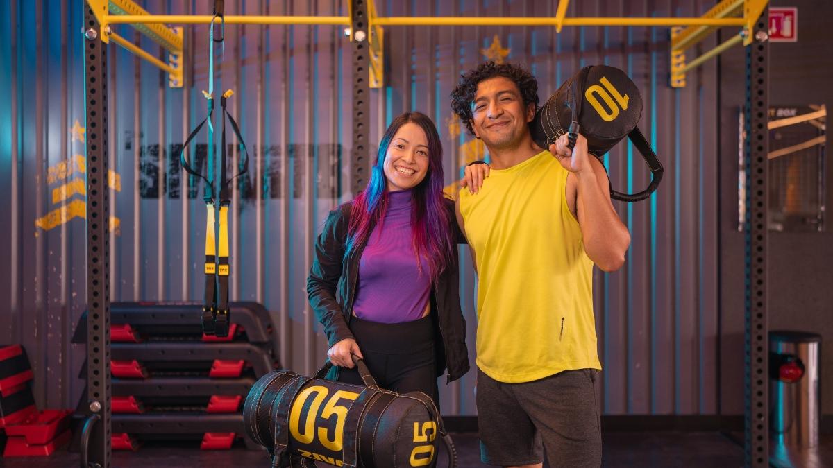 Hombre y mujer sonriendo, parados dentro del área de Smart Box cargando un costal de peso