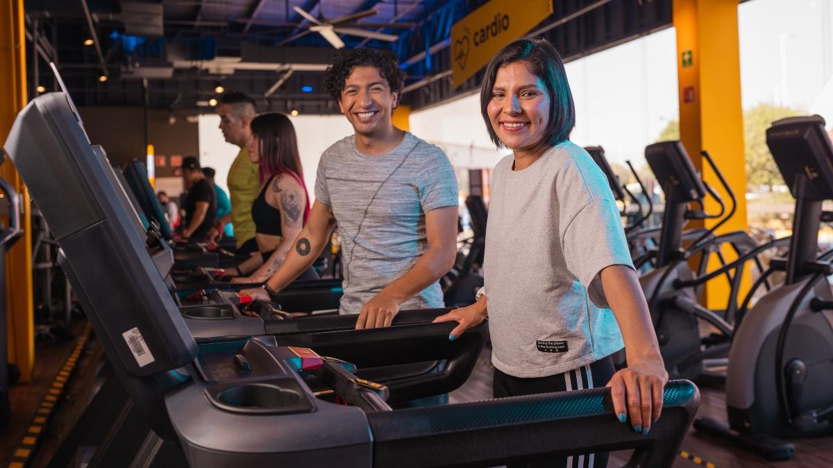 Hombre y mujer parados sobre una caminadora, volteando a la cámara con un sonrisa en el rostro