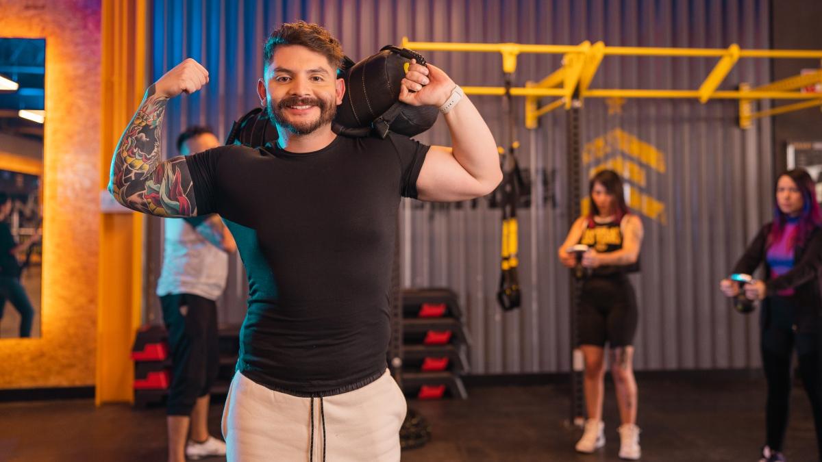 hombre de pie con los brazos flexionado mostrando sus biceps y con un costal en el hombro