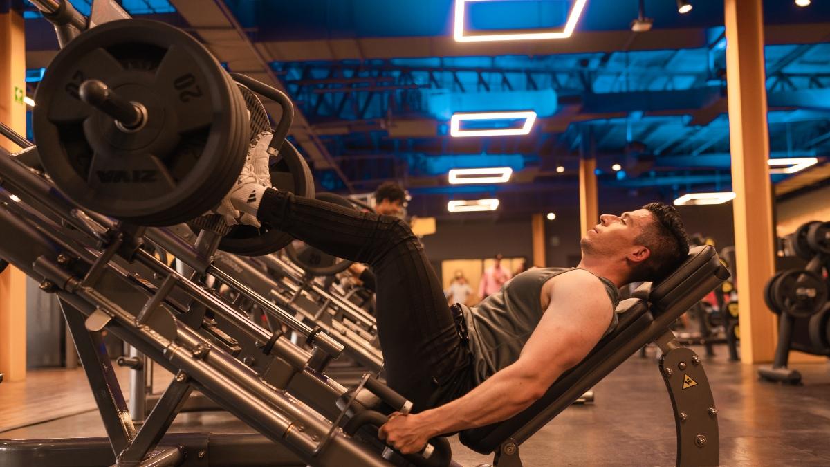 hombre sentado en una prensa del gym, realizando ejercicio de pierna