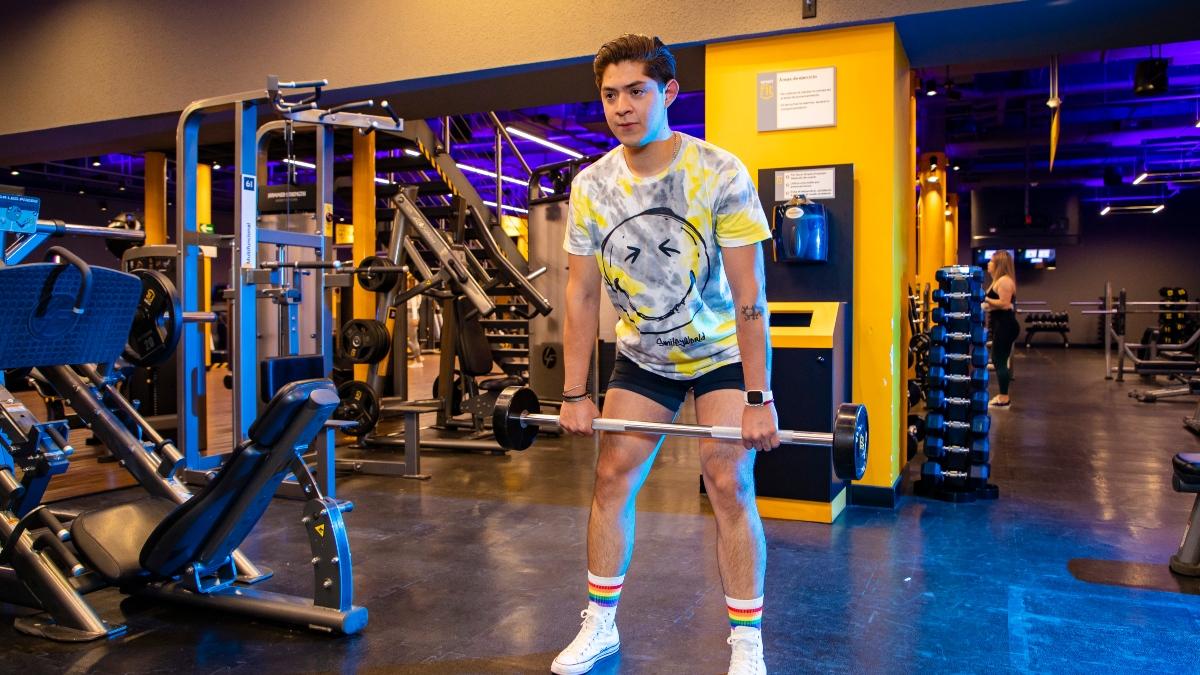 Hombre joven con una barra en las manos, realizando un peso muerto rumano en el gimnasio Smart Fit