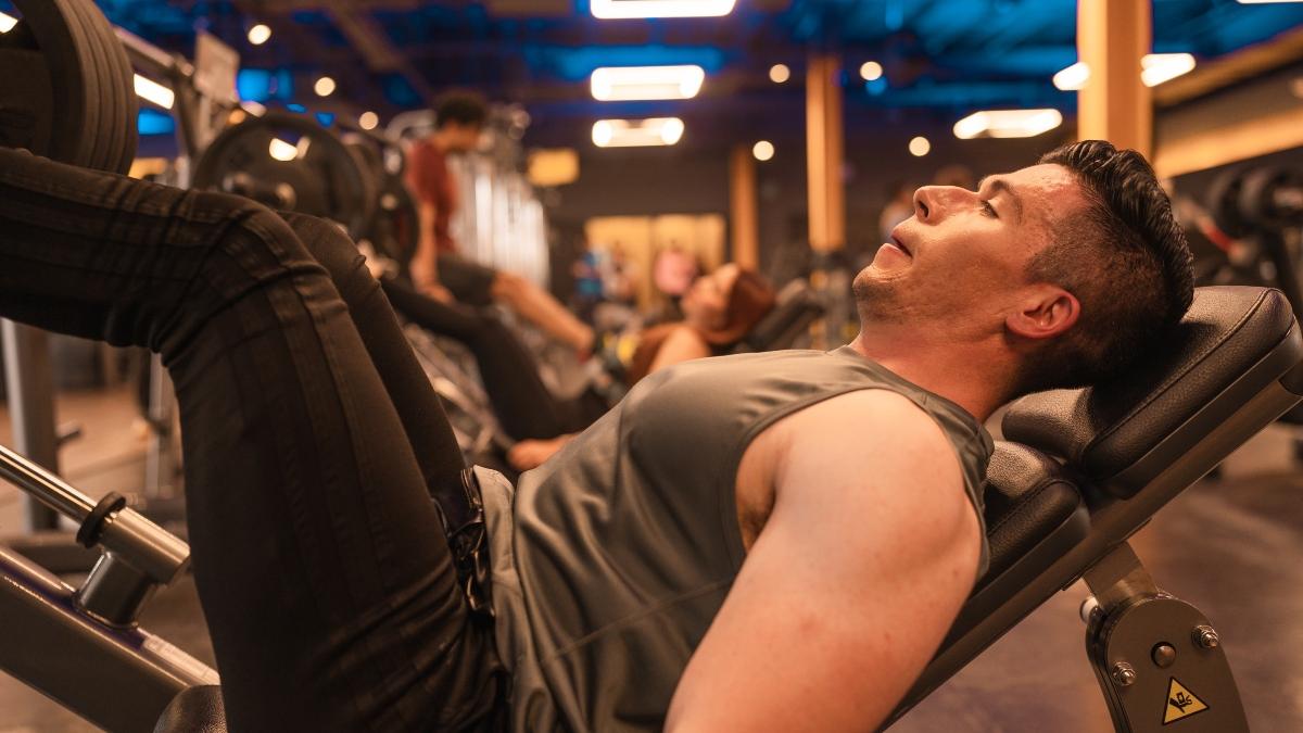 hombre recostado en una prensa del gym, realizando ejercicio controlando su respiración