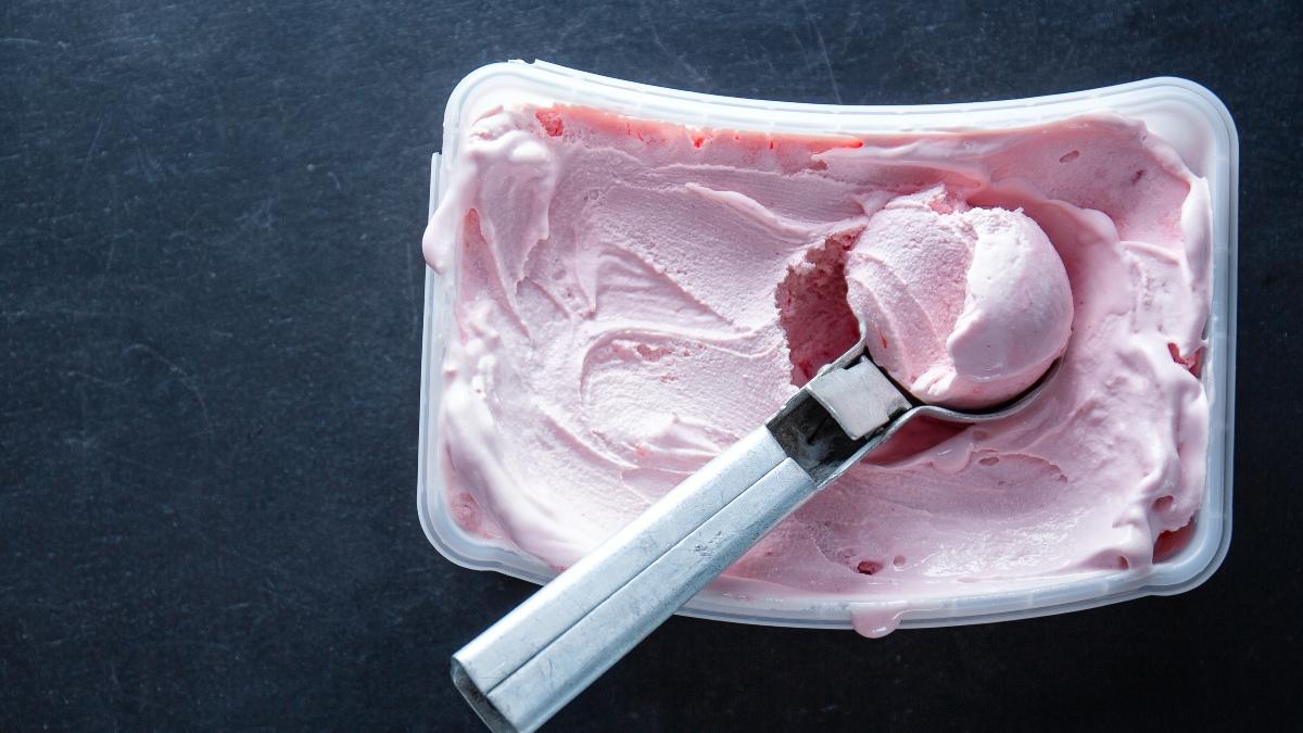 Molde de forma rectangular con helado de color rosa y una cuchara para servir