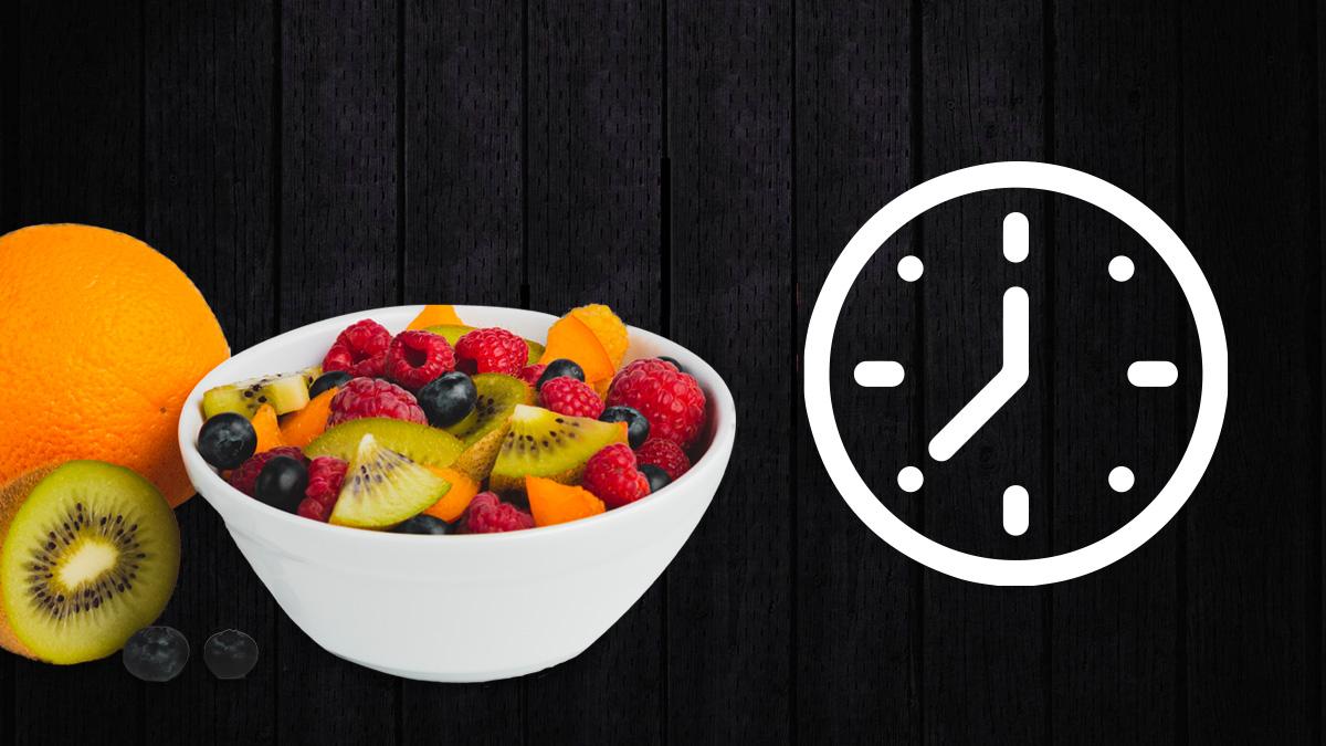 Bowl de frutas con pedazos de kiwi, frambuesas, arándanos y naranja. A un lado una naranja completa, un kiwi a la mitad y dos arándanos. Del otro lado un reloj.