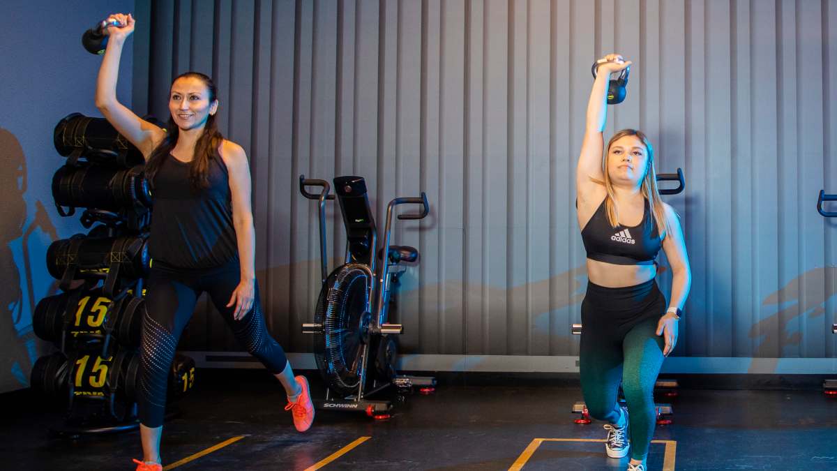 Dos mujeres realizando un ejercicio con una pessa rusa en la mano. En un gimnasio Smart Fit.