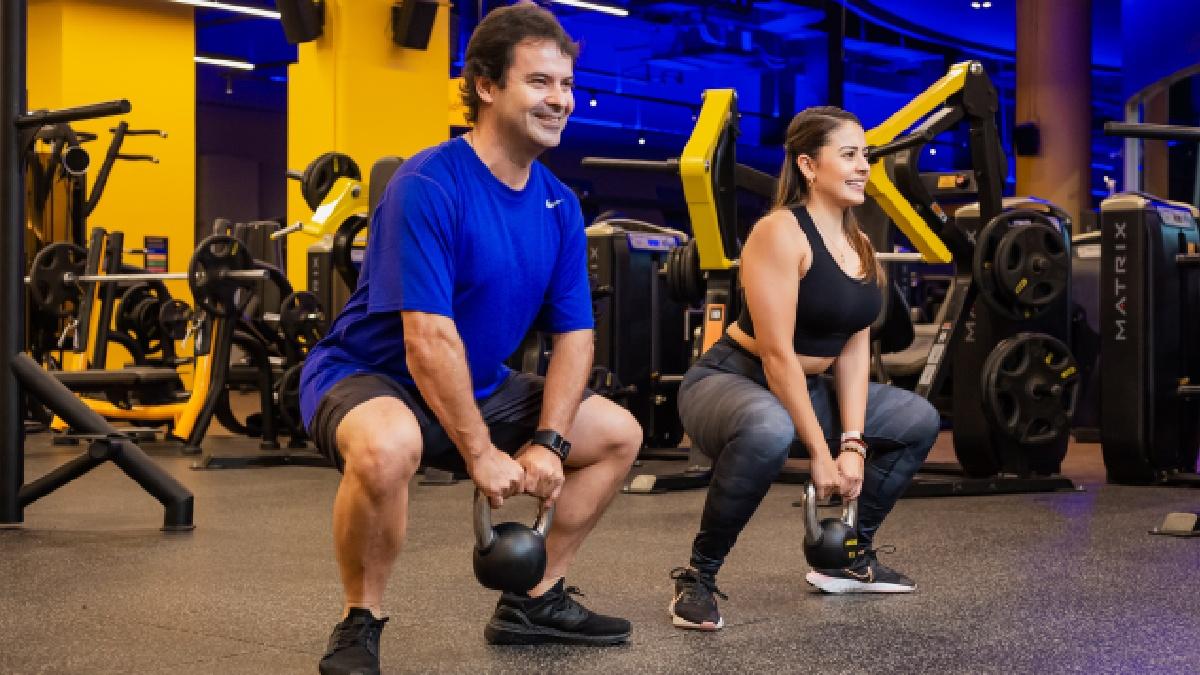 hombre y mujer realizando una sentadilla sumo con una pesa rusa, en el área de Smart Box de un gimnasio Smart Fit.