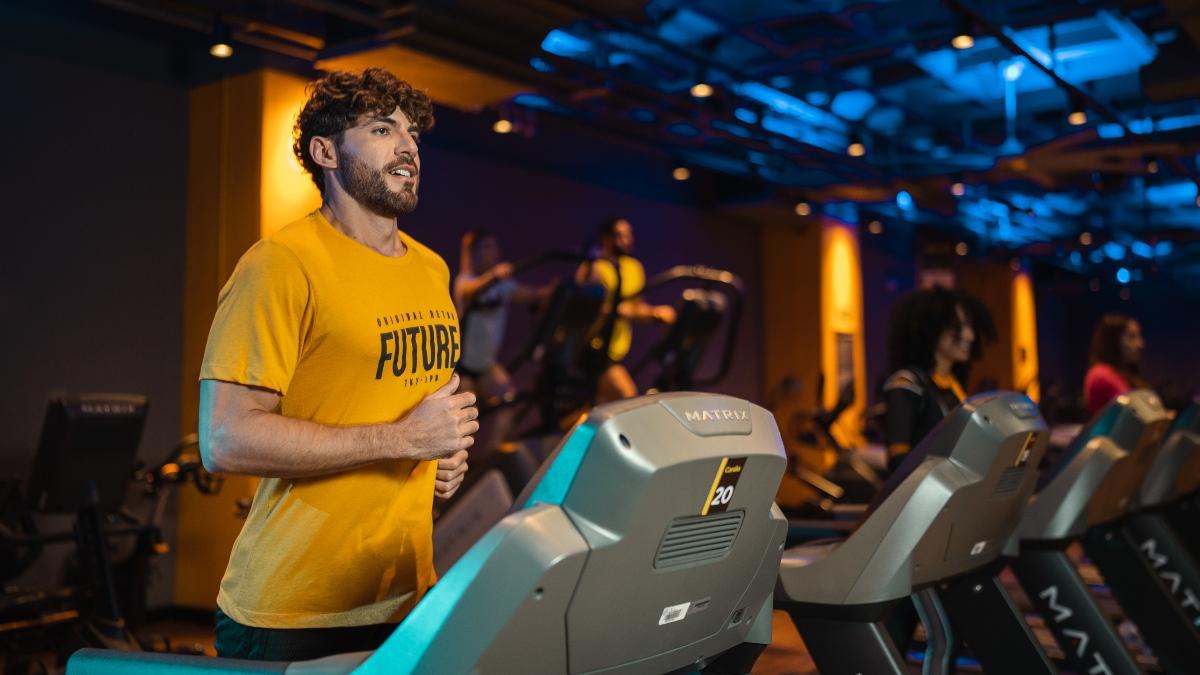 Persona corriendo en una caminadora dentro de un gimnasio Smart Fit, ambiente moderno y dinamico con iluminacion calida, ideal para realizar ejercicios que ayudan a calmar la ansiedad.