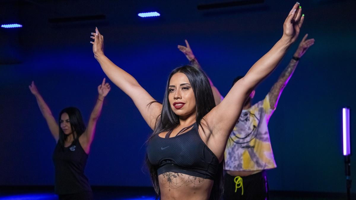 torso de una mujer levantando los brazos, haciendo ejercicio dentro de un salón de clases de un gimnasio Smart Fit