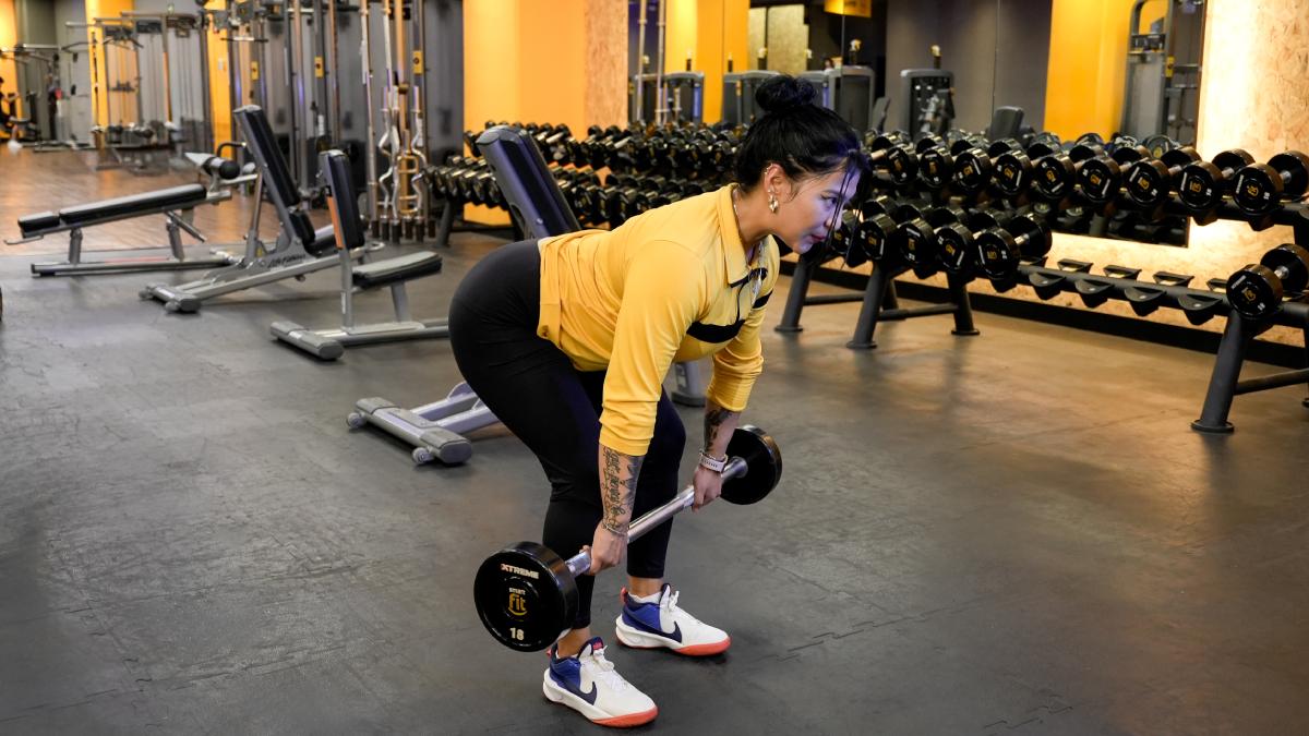 mujer con el torso inclinado hacia adelante sosteniendo una barra con las dos manos