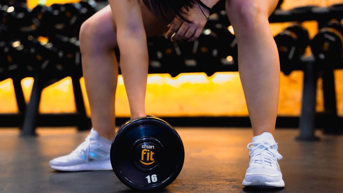piernas de una mujer flexionada y un brazo estirado levantando una mancuerna del suelo