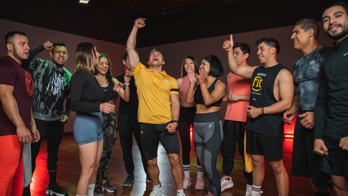 grupo de personas reunidas alrededor de un profesor del gimnasio Smart Fit aplaudiendo y levantando los brazos en señal de celebración.