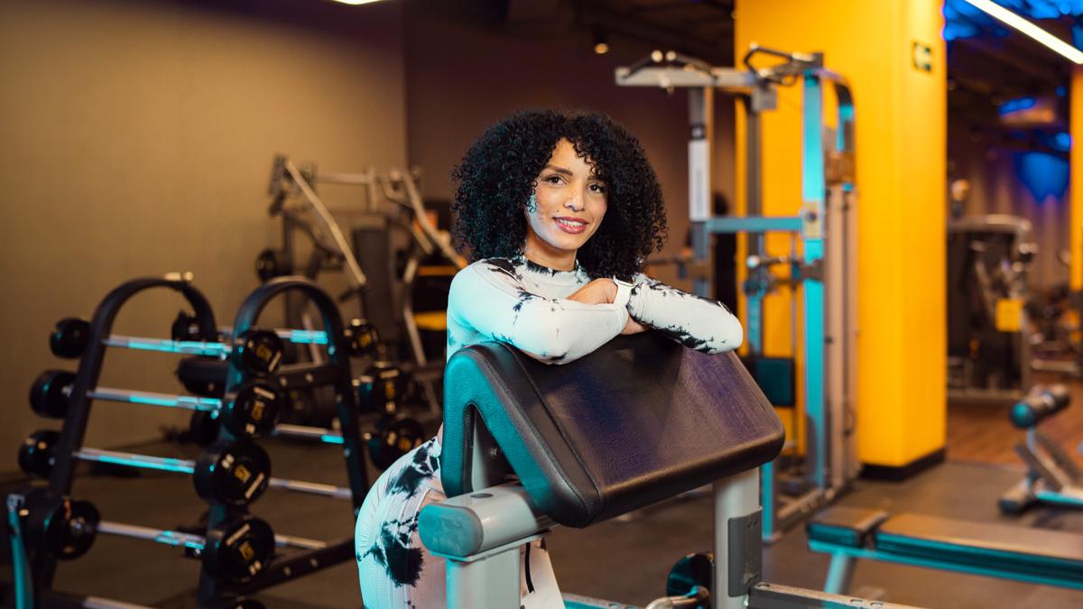 mujer de perfil colocada en un banco scott, con los brazos cruzados y recargados sobre el banco