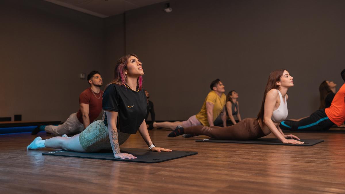 Personas participando en una clase grupal enfocada en flexibilidad y estiramiento en gimnasios Smart Fit, utilizando colchonetas en un ambiente tranquilo y espacioso