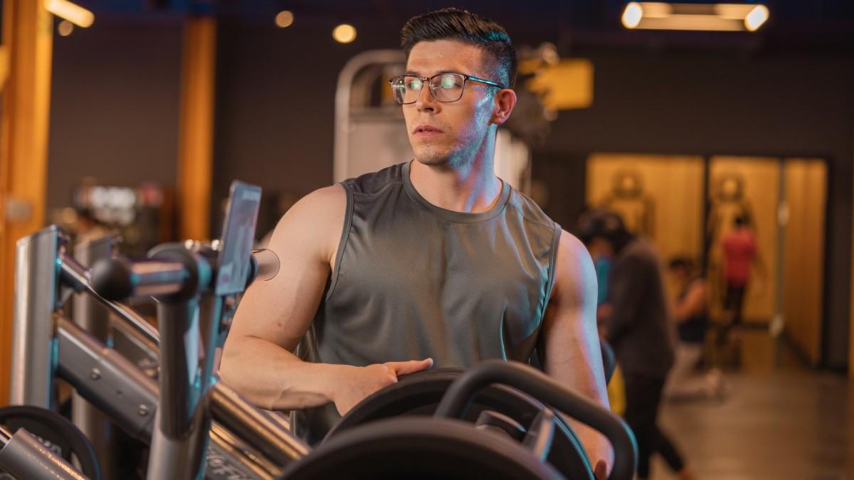 torso de un hombre de frente, con la cabeza girada hacia un lado. En las manos sostiene un disco que colocará en una prensa del gimnasio