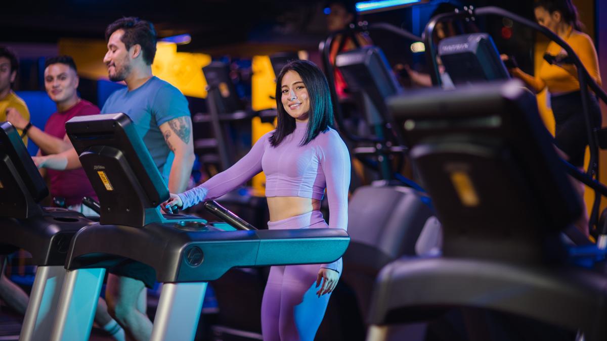 mujer parada sobre una caminadora de un gimnasio Smart Fit con una mano sobre el agarre