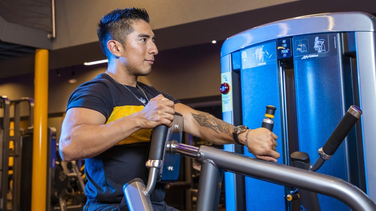 torso de un hombre de perfil, sentado sobre una maquina del gimnasio para trabajar la espalda
