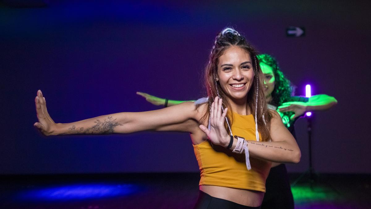torso de una mujer de frente, con una sonrisa en el rostro. un brazo estirado hacia un costado y el otro flexionado.